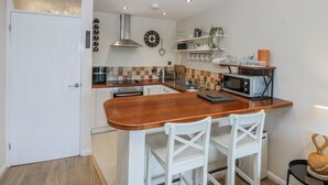 Une cuisine compacte avec un comptoir-bar en bois, des chaises blanches, un four à micro-ondes et une hotte de cuisine en acier inoxydable.