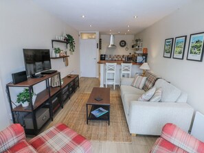Una sala de estar moderna con un sofá, una mesa de centro y un televisor. Hay una zona de cocina con un microondas y un lavamanos.
