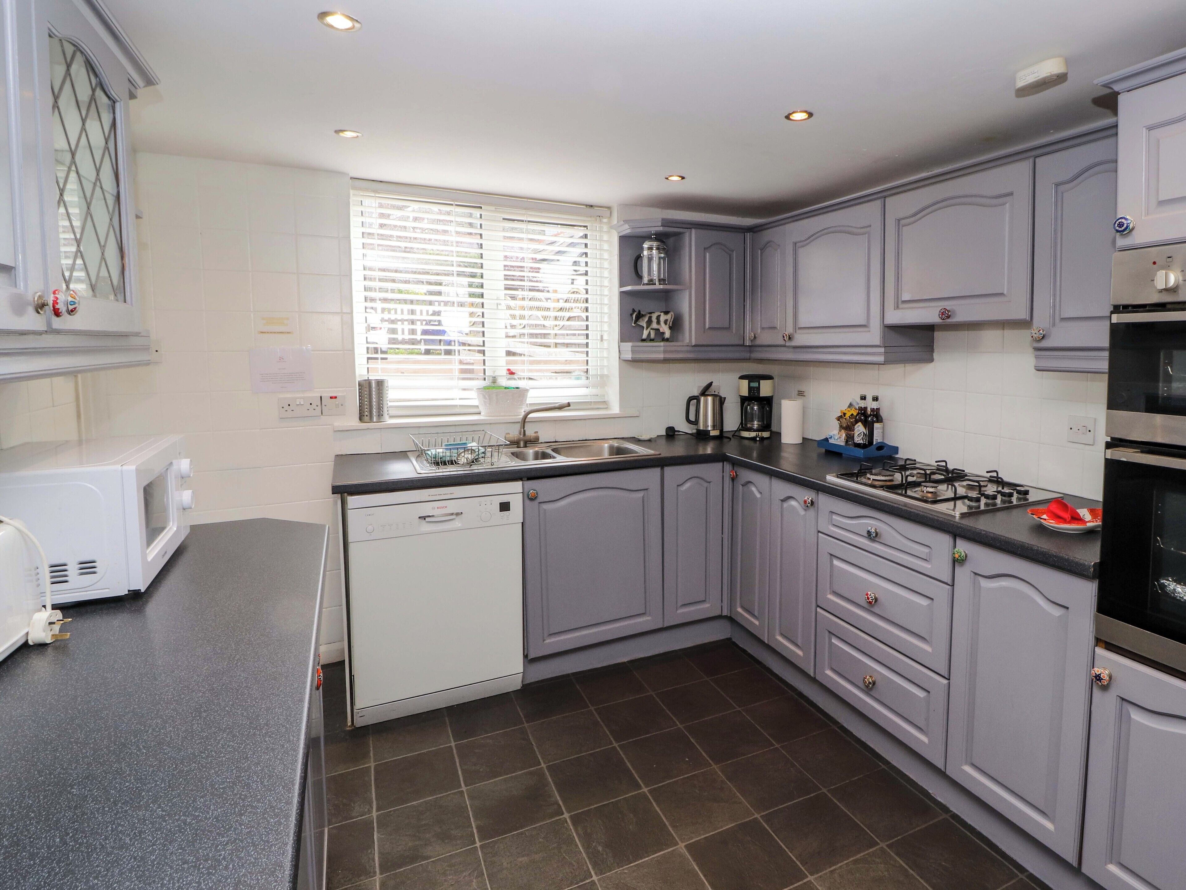 A modern kitchen with grey cabinets, a dishwasher, a sink, and a stove.