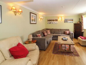 A cozy living room with a sofa, a coffee table, and a rug. There are wall-mounted lamps and framed pictures on the walls. - Brews Cottage (Keswick)