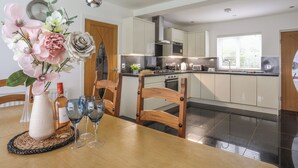 A modern kitchen with white cabinets, a wooden dining table, and a vase with flowers. - Monarfon (Criccieth)