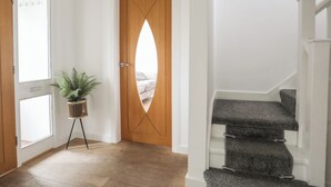 A hallway with a wooden door, a potted plant, and a staircase with carpeted steps. - Monarfon (Criccieth)