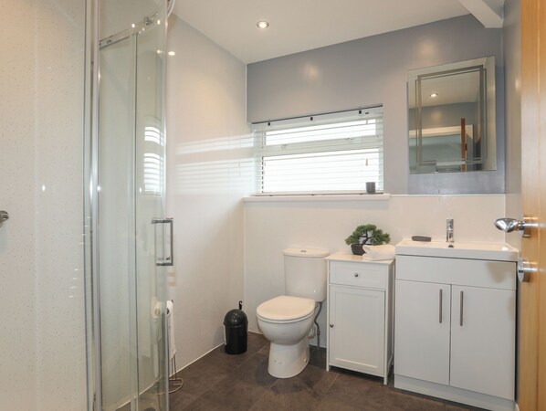 A modern bathroom with a glass shower enclosure, a toilet, a sink with a mirror above, and a cabinet with storage. - Monarfon (Criccieth)