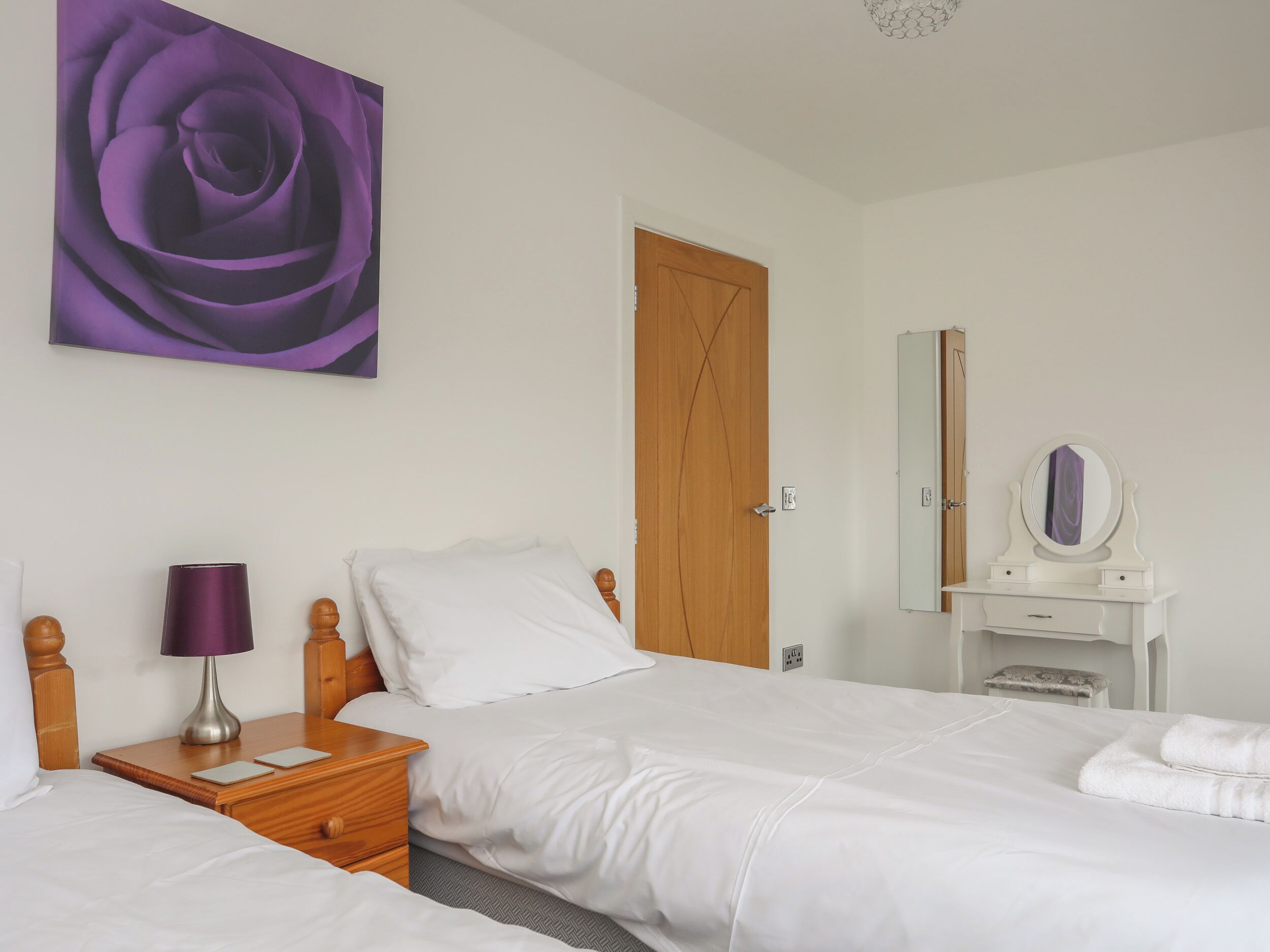 A bedroom with a bed, a nightstand, a lamp, a dresser with a mirror, and a door.