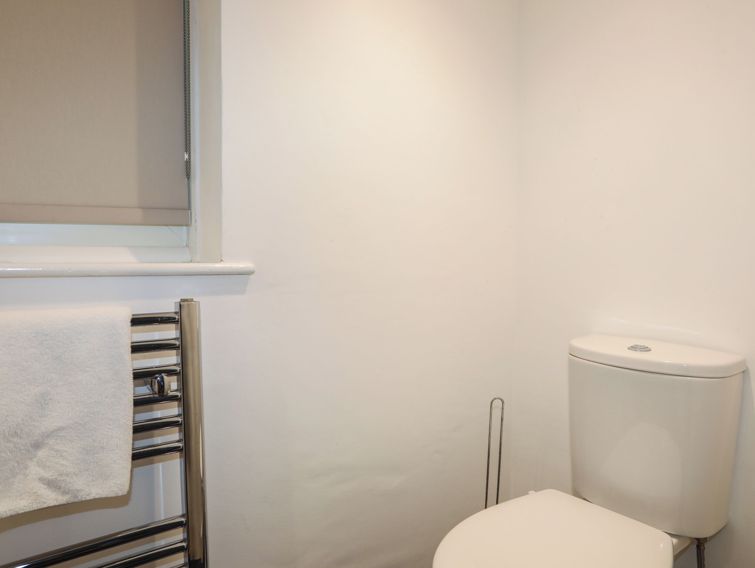 A bathroom with a white toilet, a towel rack with a white towel, and a window with blinds.
