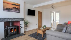 A living room with a fireplace, a sofa, a television, and a view of the outdoors. - Monarfon (Criccieth)