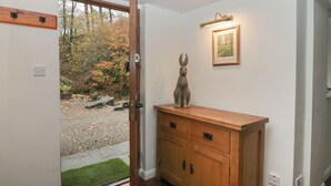 A wooden cabinet with drawers, a framed picture on the wall, and a door leading to an outdoor area with a gravel path and greenery.
