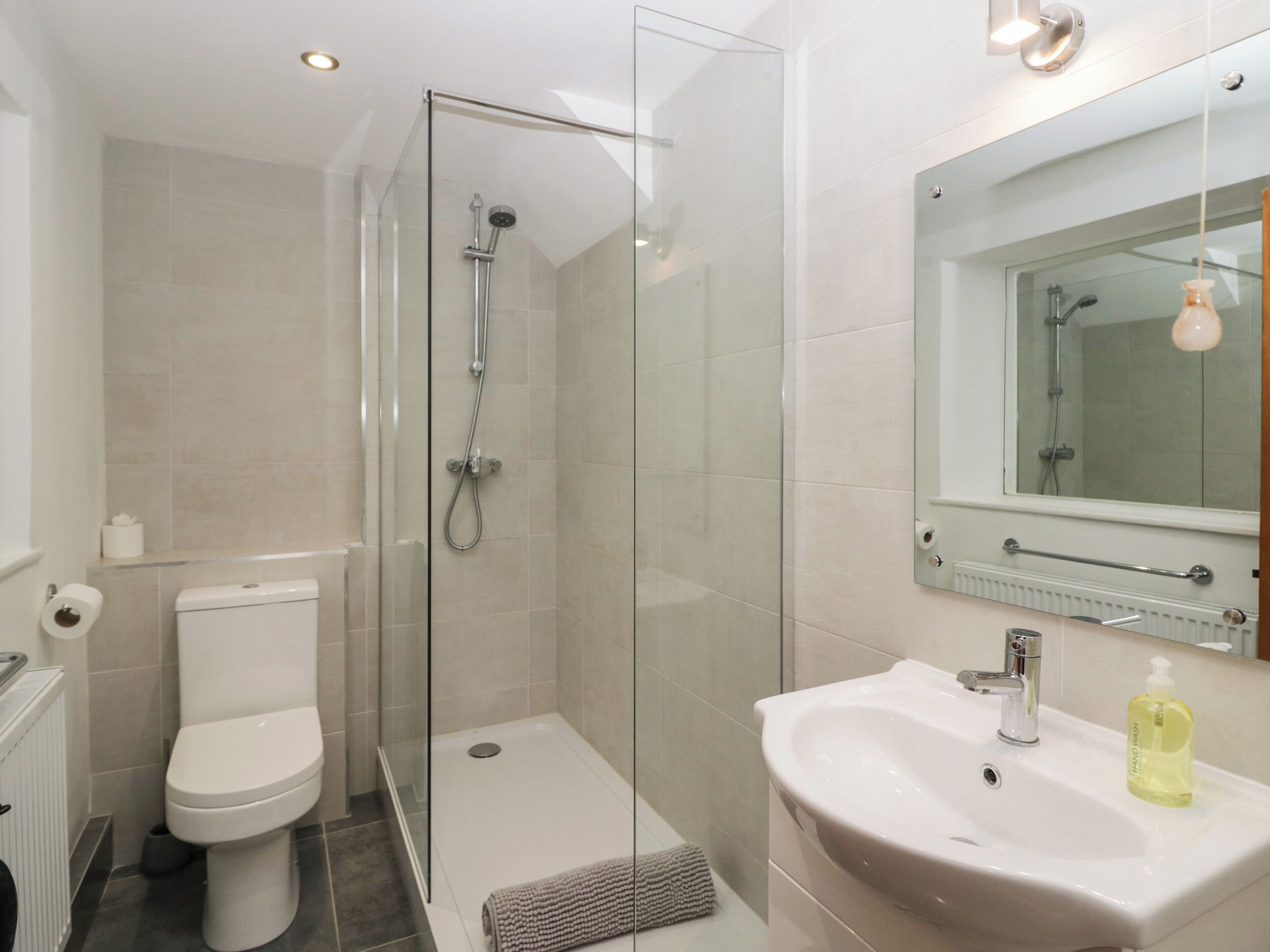 A modern bathroom with a glass-enclosed shower, a toilet, and a sink with a mirror above it.