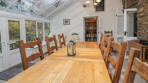 A dining area with a wooden table and chairs, a glass ceiling, and a stone wall.