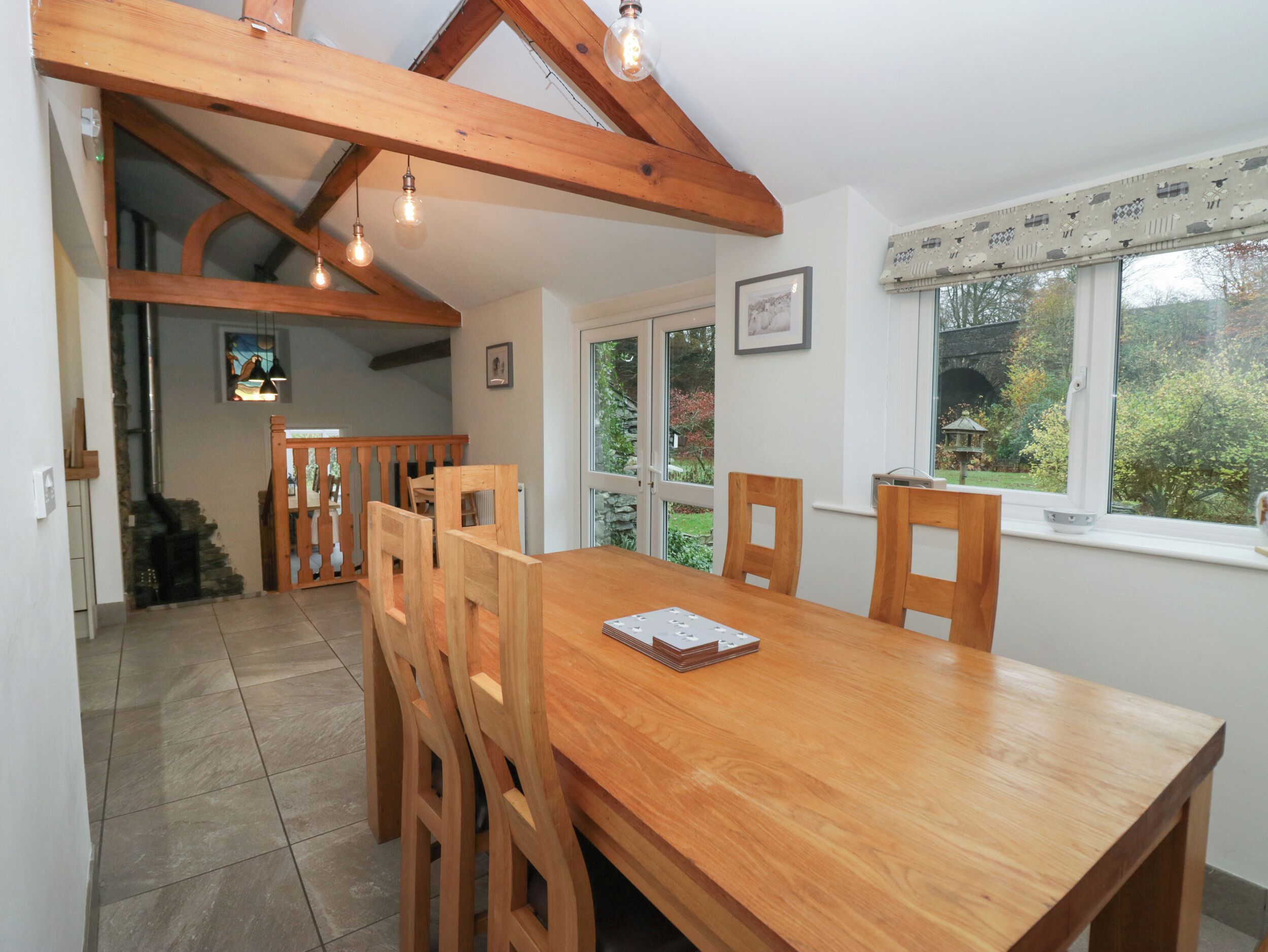 A dining area with a wooden table and chairs, a staircase leading to another room, and a window with a view of greenery.