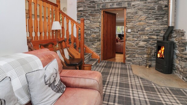 A cozy living room with a stone wall, a fireplace, a wooden staircase, and a plush sofa.