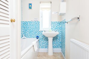 A bathroom with a white bathtub, a sink, and a window with a curtain.