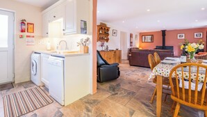 A kitchen with a washing machine, a dining area with a table and chairs, and a living area with a sofa and a fireplace. - Cothi Cottage (Cardigan)