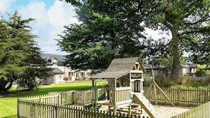 A playground with a wooden play structure, surrounded by a wooden fence and a grassy area. - Cothi Cottage (Cardigan)