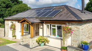 A stone building with a sloped roof, solar panels, and potted plants. - Cothi Cottage (Cardigan)