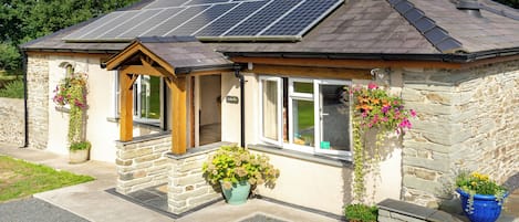 A stone building with a sloped roof, solar panels, and potted plants.