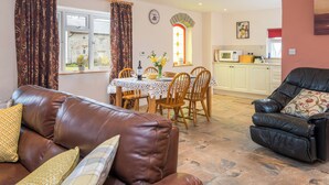 A living room with a brown leather sofa, a dining table with chairs, a kitchen area, and a black leather armchair. - Cothi Cottage (Cardigan)