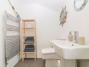 Un baño con un lavamanos blanco, inodoro y un estante de madera con toallas dobladas.