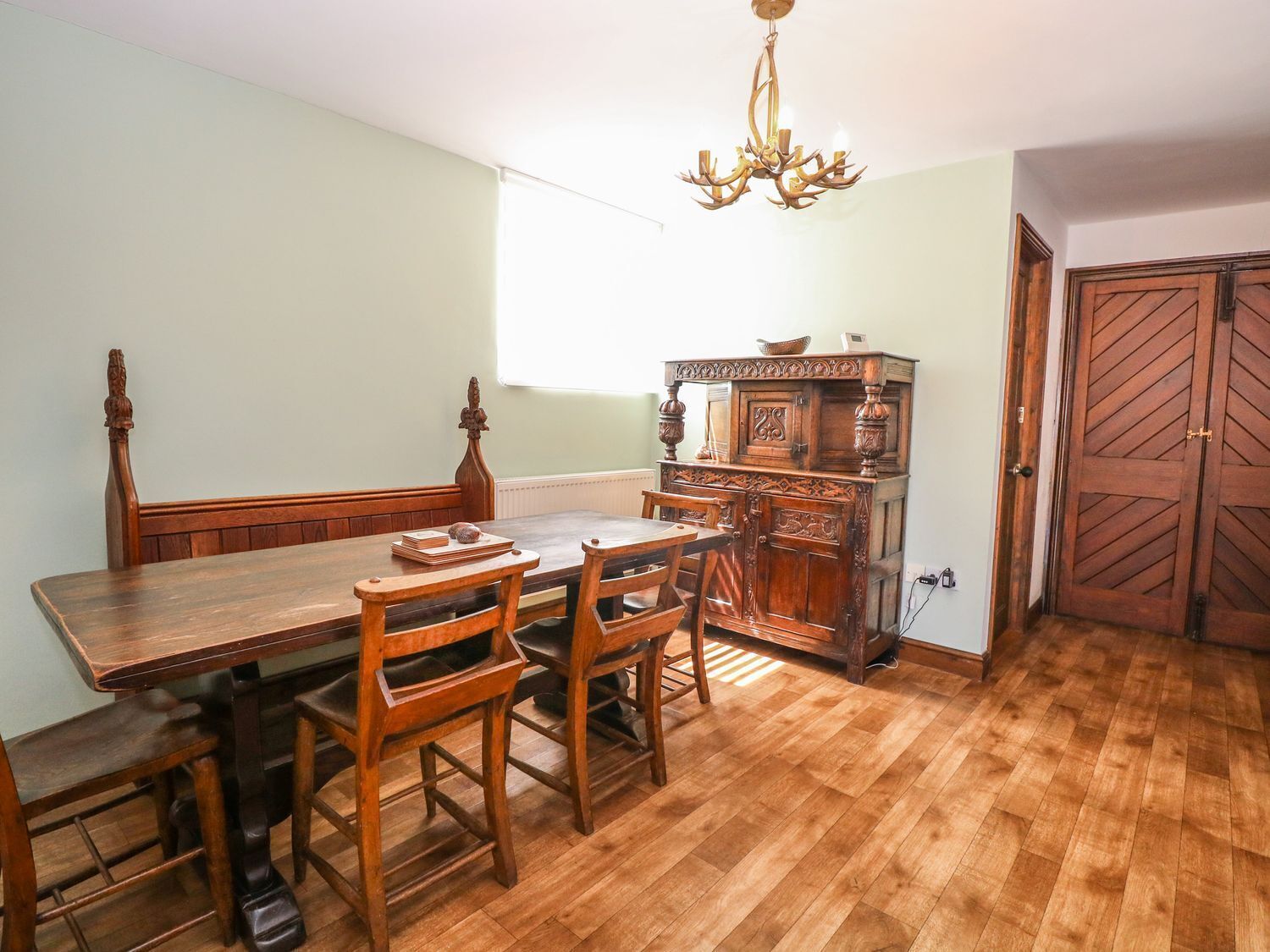 A dining room with a wooden table and chairs, a chandelier, and a wooden cabinet.