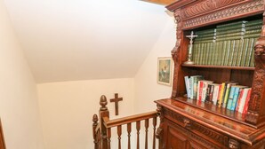 A wooden staircase with a railing, a wooden bookcase with books, and a wooden cross on the wall. - The Old Chapel (Dereham)