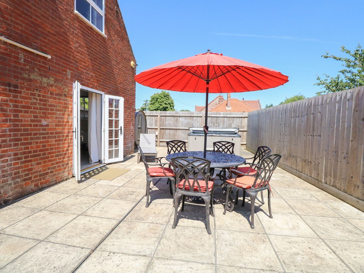 A patio with a table and chairs, a red umbrella, and a brick wall.