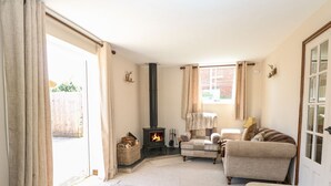 A cozy living room with a fireplace, comfortable seating, and a large window. - The Old Chapel (Dereham)
