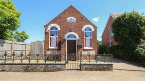 A brick building with a triangular roof, arched windows, and a door. There is a sign above the door that reads "Primitive Methodist Church." - The Old Chapel (Dereham)