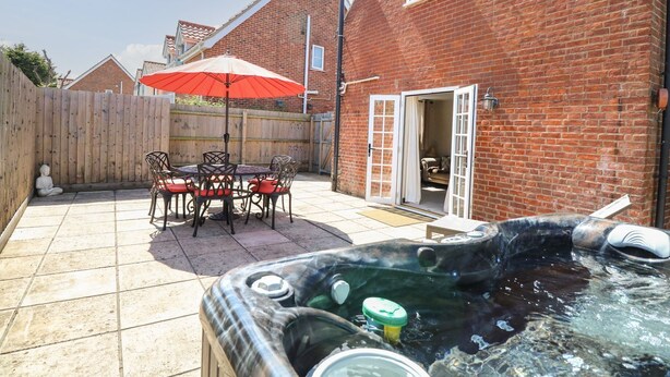 A backyard with a hot tub, a wooden table with chairs, and a red umbrella. - The Old Chapel (Dereham)
