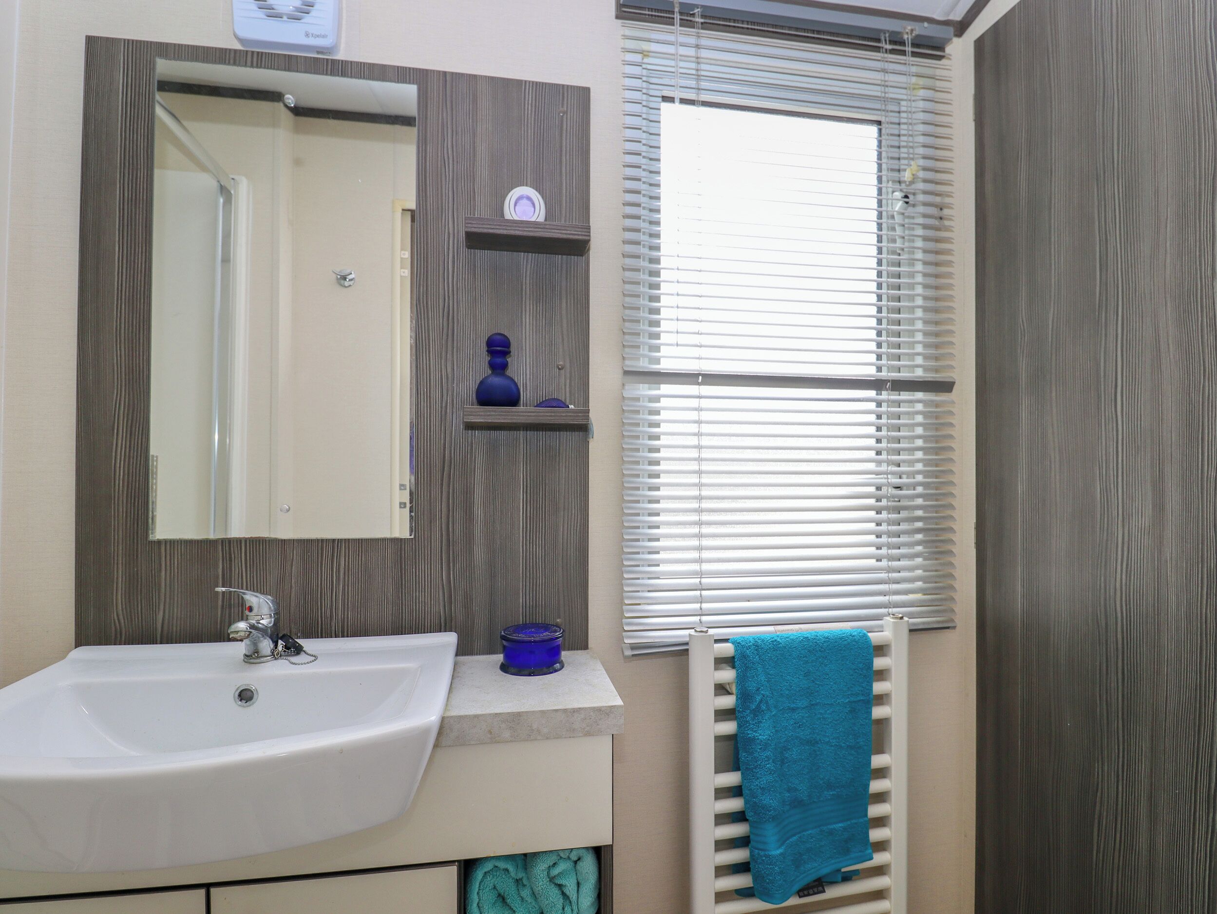 A bathroom with a white sink, a mirror, a towel rack with a blue towel, and a window with blinds.