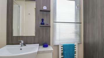 A bathroom with a white sink, a mirror, a towel rack with a blue towel, and a window with blinds.