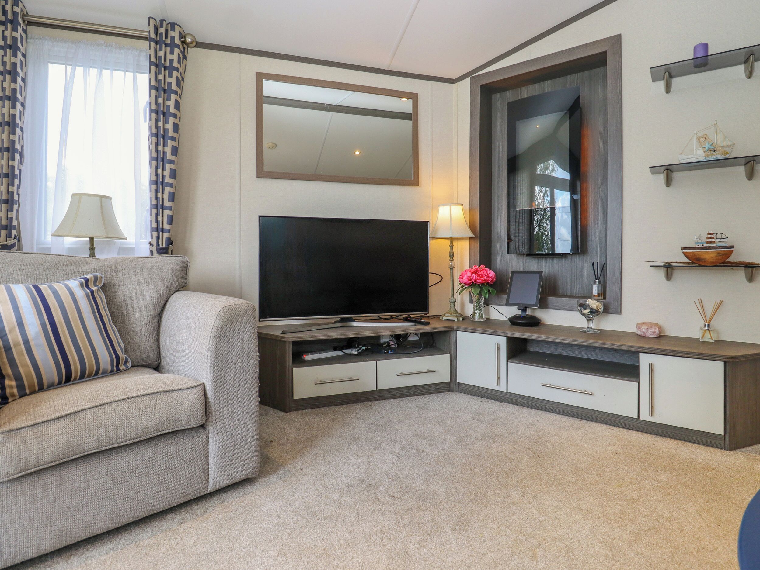 Een woonkamer met een flatscreen televisie, een bank, een salontafel en een tv-meubel met een spiegel en planken.