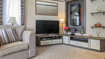 Een woonkamer met een flatscreen televisie, een bank, een salontafel en een tv-meubel met een spiegel en planken.