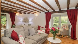 Un salon chaleureux avec un canapé gris, des coussins rouges, une petite table d’appoint blanche et un fauteuil à bascule.