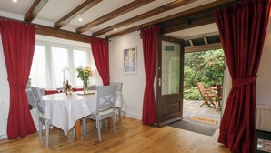 Un coin repas avec un plancher en bois, une table recouverte d’une nappe blanche et des rideaux rouges.