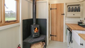 A cozy kitchen with a wood-burning stove, a window with a view, and a door leading to another room. - Spindle (Witney)