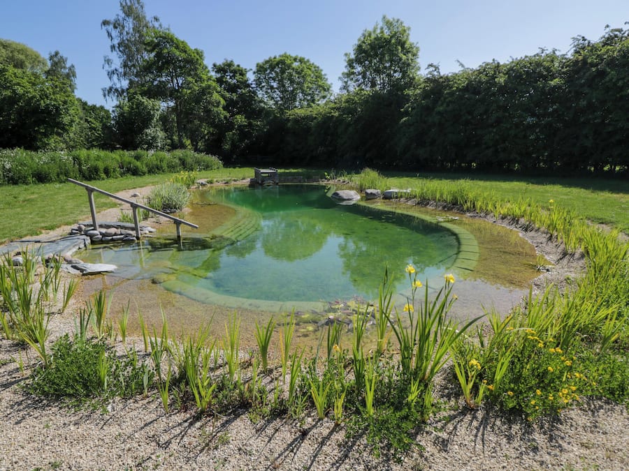 A circular pond with a stone bridge, surrounded by greenery and trees.