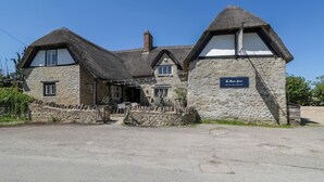 A traditional stone building with a thatched roof, a sign indicating it is a pub, and a stone wall in front. - Spindle (Witney)