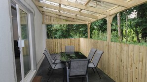 A covered patio with a table and chairs, a wooden fence, and a door leading to a room. - Ciara's Place (Riverstown)