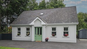 A white house with a green door, two windows with flower boxes, and a grey roof. - Ciara's Place (Riverstown)