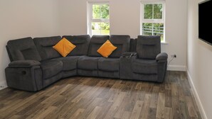 A modern living room with a sectional sofa, two windows, and a flat-screen TV mounted on the wall. - Ciara's Place (Riverstown)