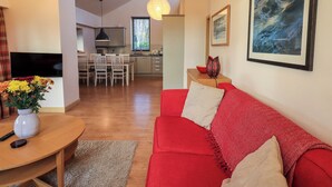 Een moderne woonkamer met een rode bank, een houten eettafel en een aan de muur bevestigde televisie.