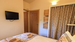 Een slaapkamer met een bed, een aan de muur bevestigde televisie, houten deuren en rieten manden aan de wand.