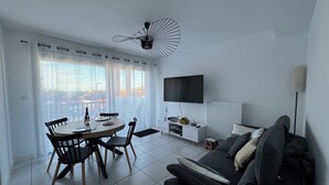 Ein modernes Wohnzimmer mit Essbereich, einem schwarzen Sofa, einem Fernseher und einem Deckenventilator.