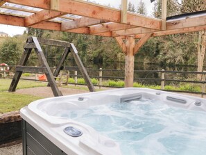 A hot tub under a wooden pergola with a wooden ladder nearby, surrounded by greenery and a body of water. - 4 Carlton Cottages (Enniskillen)
