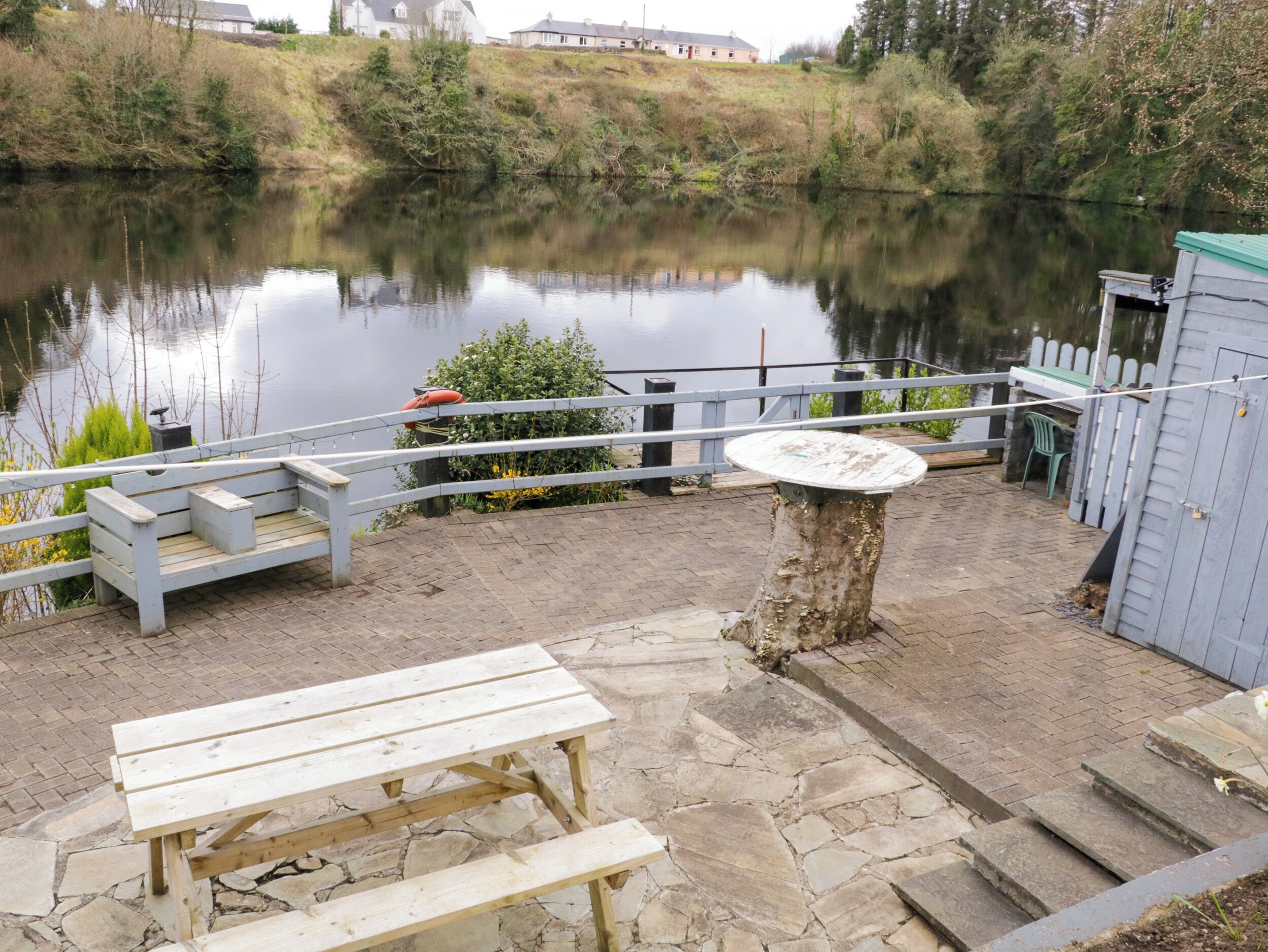 Ein Picknickplatz am Seeufer mit einer Holzbank und einem Tisch, umgeben von einer Steg-Terrasse und einem Holenzaun.