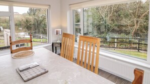 A dining area with a table, chairs, and a view of a garden through large windows. - 4 Carlton Cottages (Enniskillen)