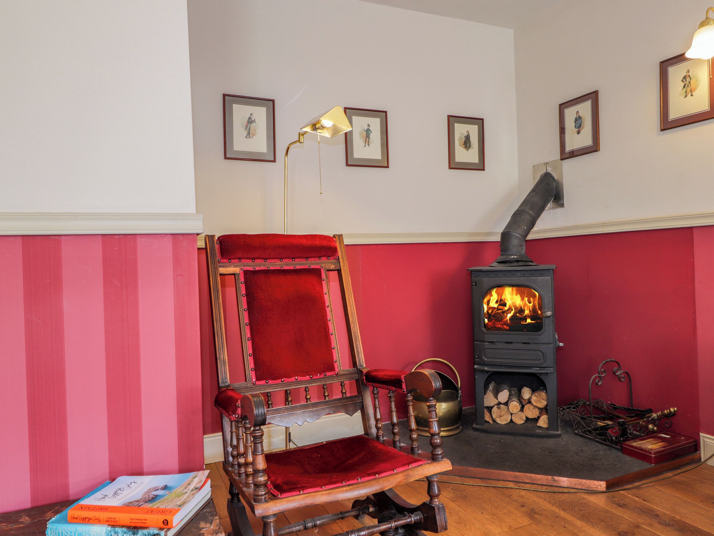 A cozy room with a red chair, a wooden table, a fireplace, and framed pictures on the wall.
