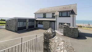 A two-story house with a stone facade, a garage, and a stone wall in the foreground. - Melin Y Plas (Barmouth)