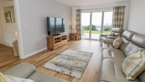 A modern living room with a leather sofa, a wooden entertainment unit, a flat-screen TV, and a large sliding glass door leading to a balcony. - Melin Y Plas (Barmouth)