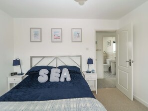 Un dormitorio con cama, mesitas de noche y un baño visible a través de una puerta abierta.